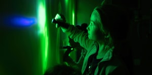 A girl using a flashlight in a room lit with green light.