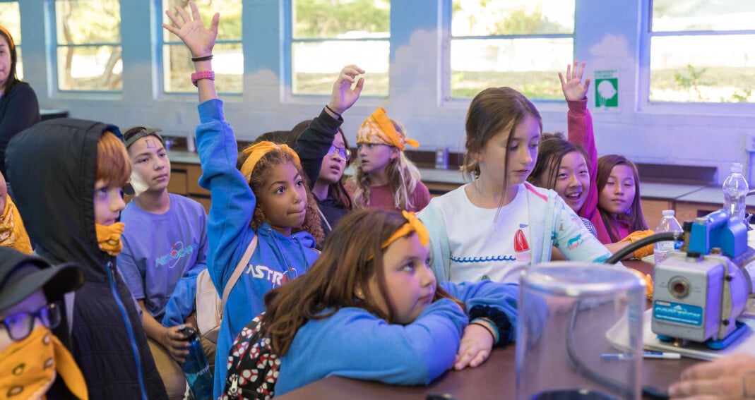 Kids in classroom raising hands.