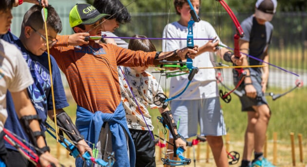 Group of campers lined up at the archery range, learning technique and aiming at targets