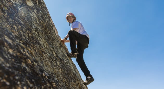 Focused camper gripping handholds while bouldering in a safe, supervised setting.