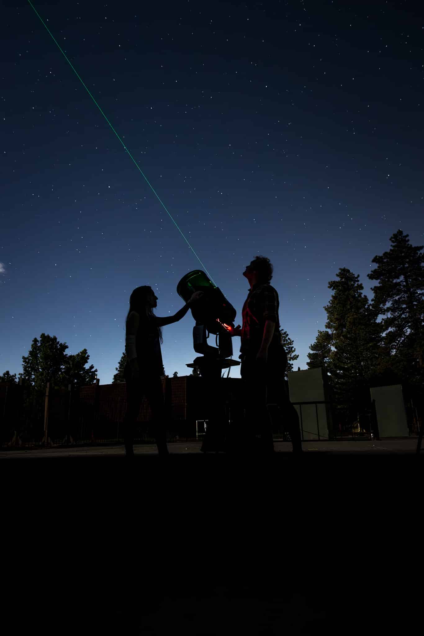 Two campers standing beside a telescope and looking up at the night sky