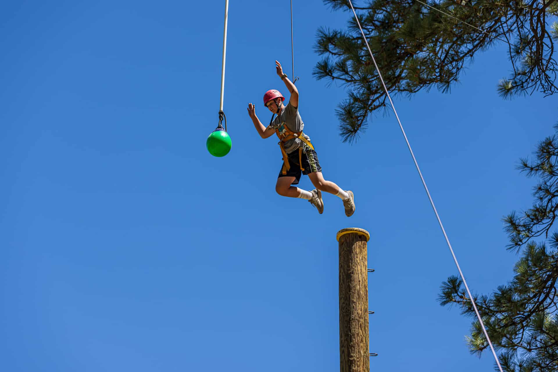 Camper leaping off the Power Pole challenge at AstroCamp high ropes course.